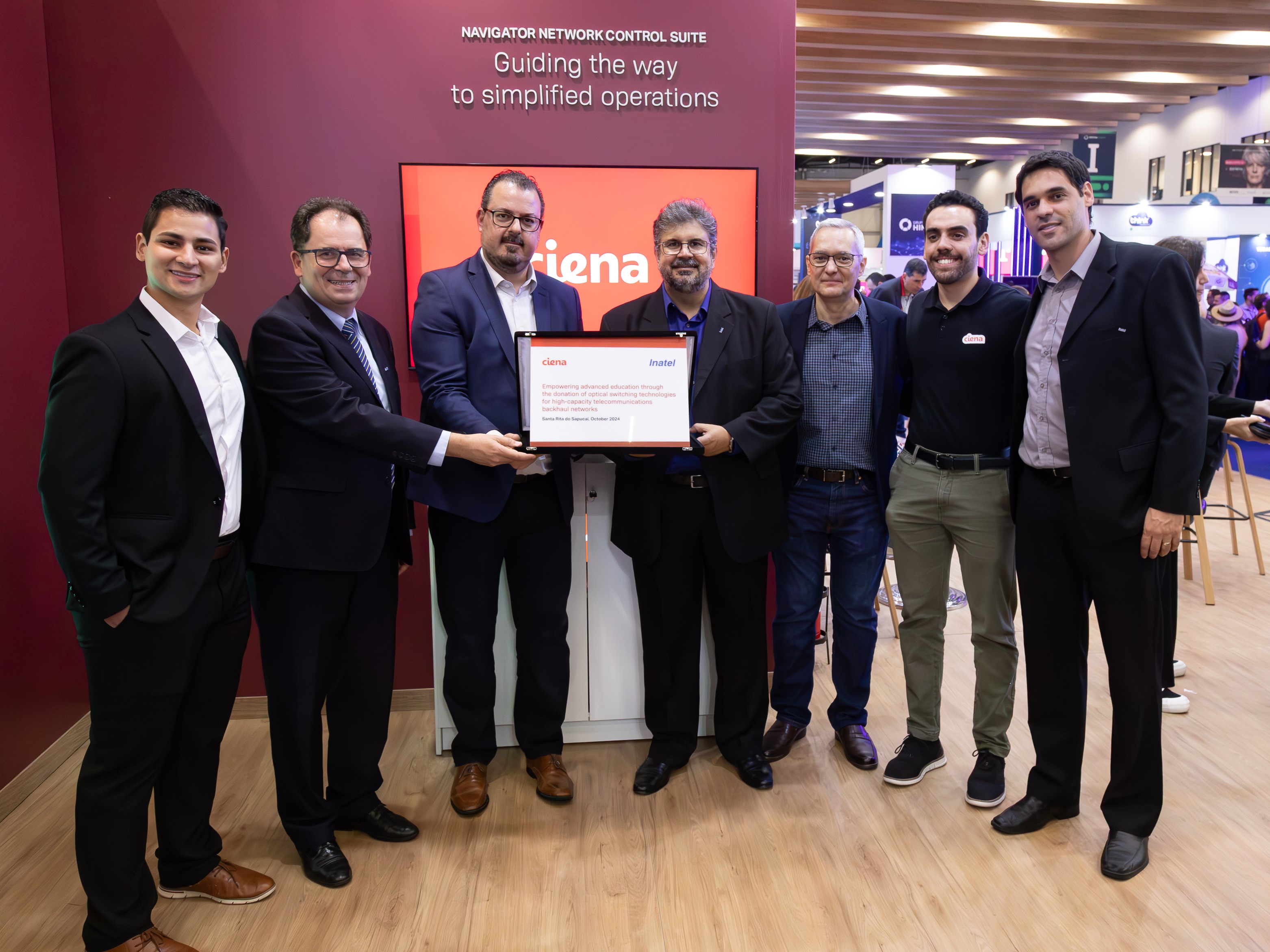 Employees from Ciena and Inatel pose with a certificate of the donation at Futurecom 2024