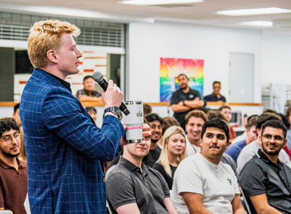 Young man speaking into a microphone in front of a group of people
