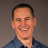 Portrait of a professional man smiling with a brown background.