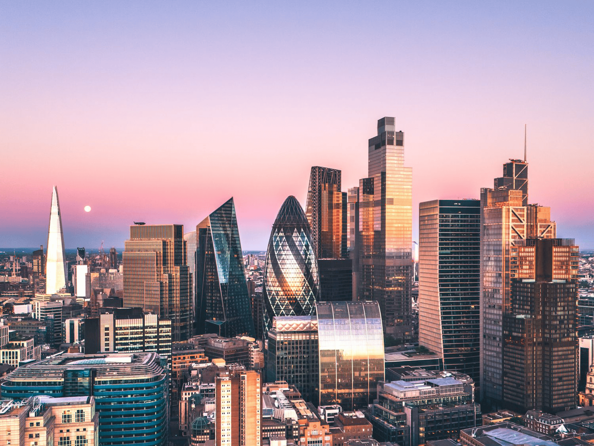 Aerial view of London’s financial district at sunset, featuring modern skyscrapers and illuminated city buildings.