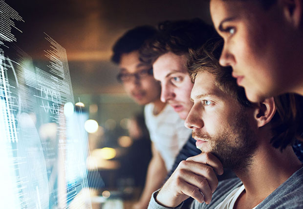 A group of people sit in front of a monitor reading over results. The lab is equipped with advanced optical and photonics equipment, symbolizing research and innovation in the field of optophotonics.