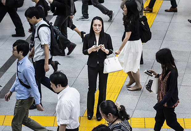 An image of people using mobile phones while walking in the subway in Japan. The image captures the busy and connected lifestyle of individuals in Japan, relying on mobile phones for communication, information, and entertainment while on the move.