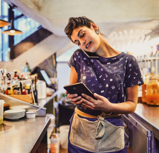 Woman in kitchen talking on phone and looking at tablet