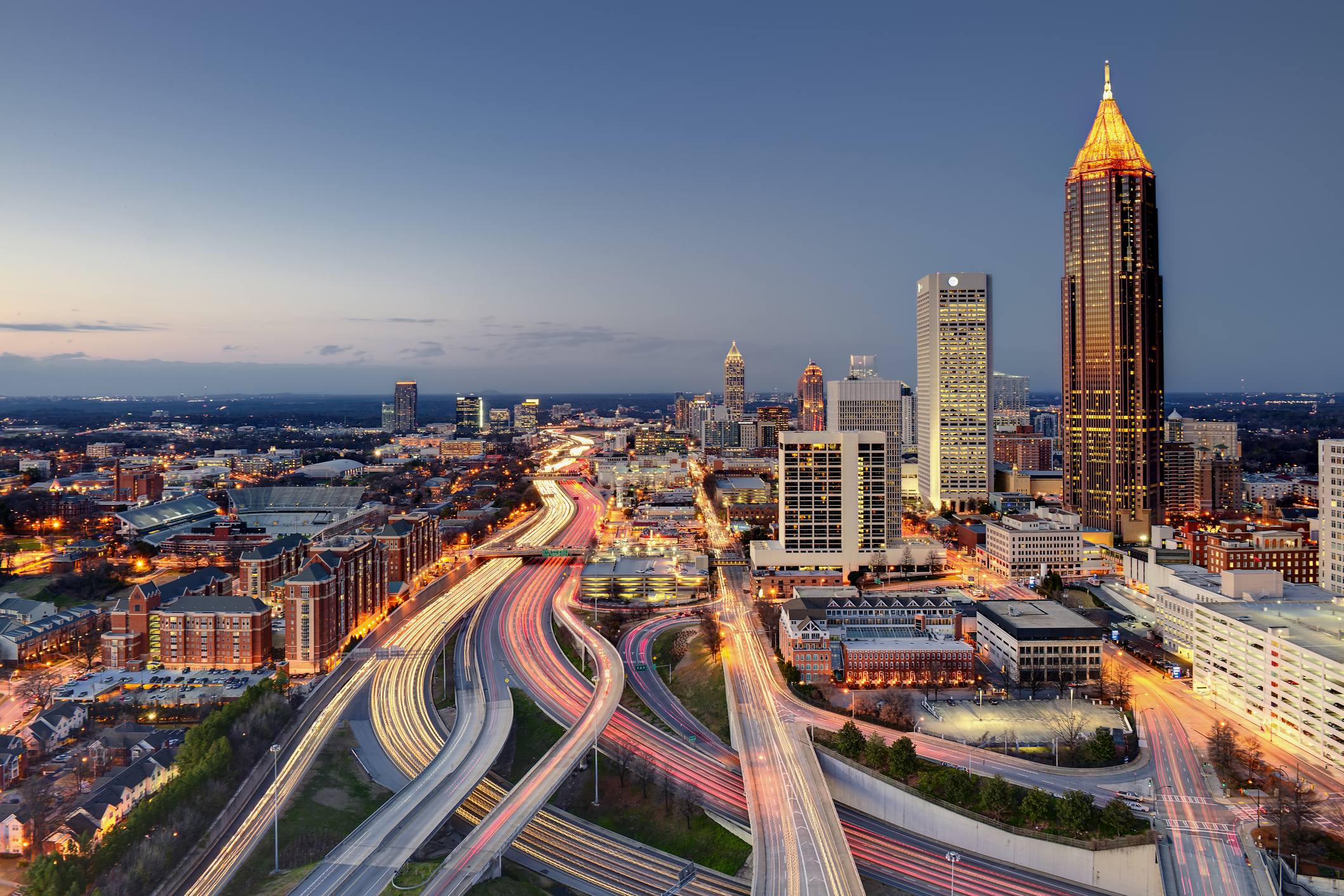 Atlanta skyline at sunset with downtown skyscrapers and highways illuminated by city lights.