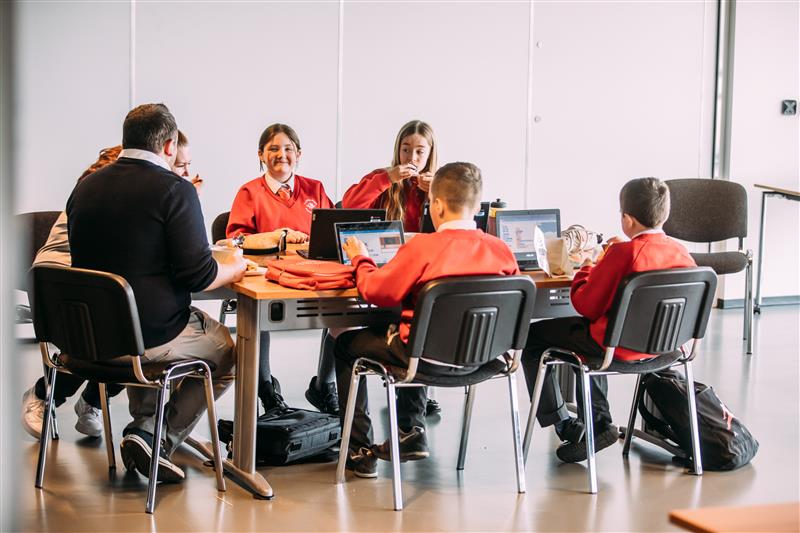 Students sit around a table working on computers