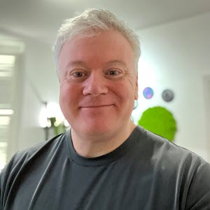 Headshot of a man smiling in a well lit white room.