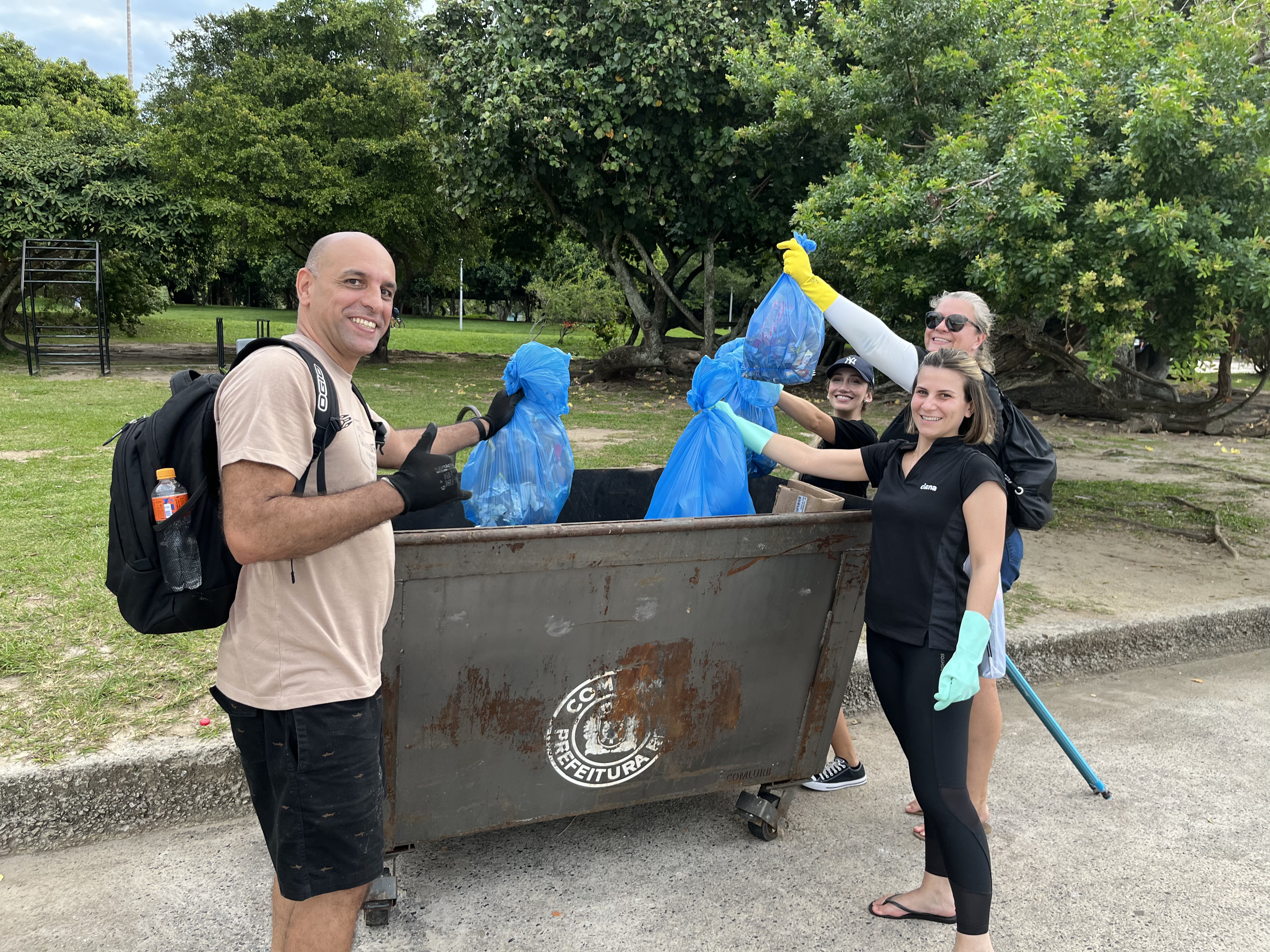 Men and women throwing trash bags in a dumpster