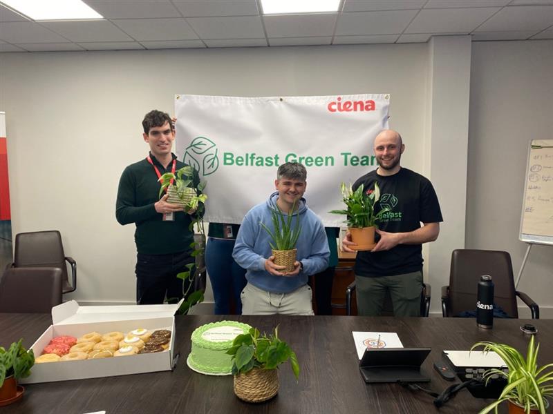 Three team members pose holding potted plants